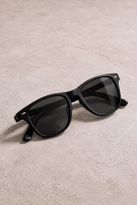 Product photo of black sunglasses on a warm beige textured surface