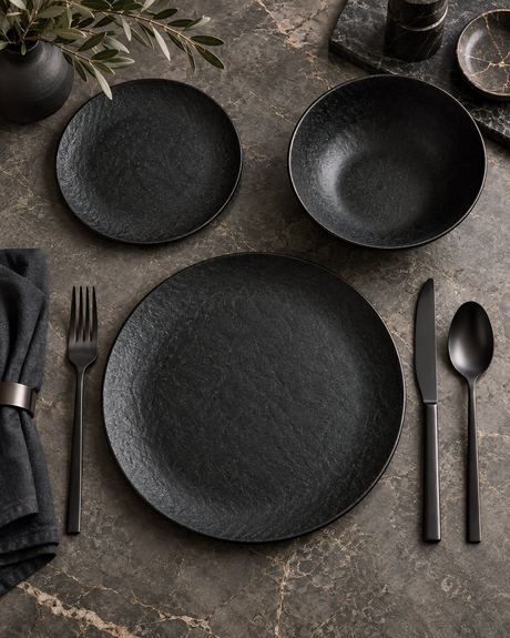 Overhead product photo of matte black plates, bowls and cutlery on dark marble