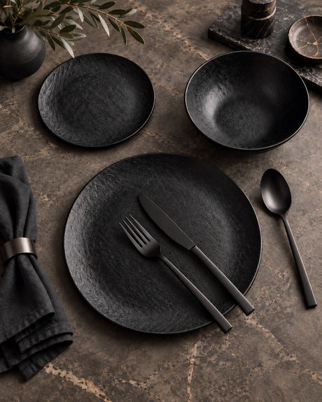 Close-up product photo of matte black plates and cutlery on dark marble