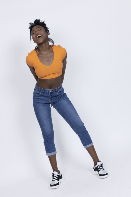 Ecommerce fashion photo of a woman in an orange crop top and cropped jeans on a white background