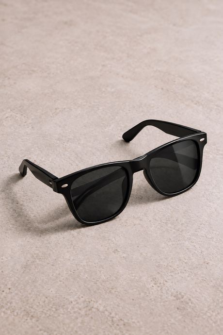 Product photo of black sunglasses angled on a beige textured surface