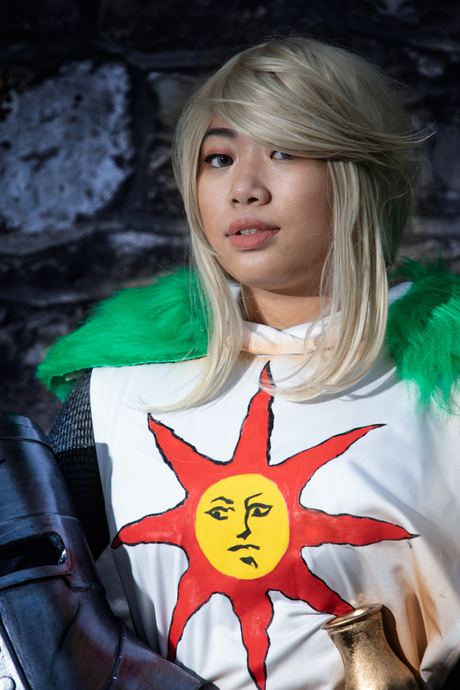 Character portrait in white armour with a sun emblem against a stone wall