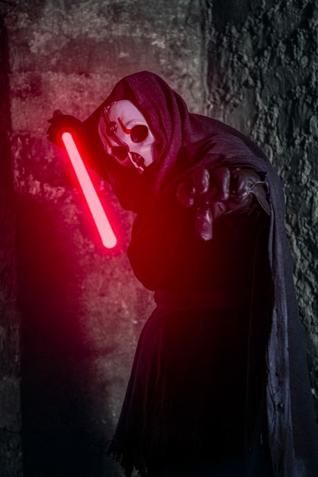 Character portrait of a hooded, masked figure lit by a glowing red blade