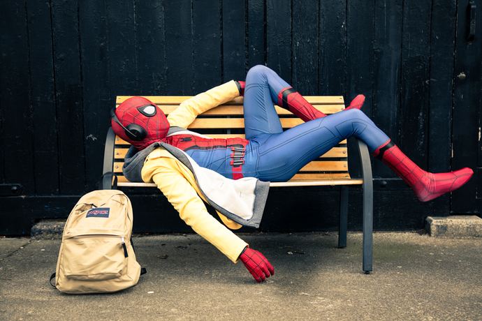 Character photo of a figure in a red and blue suit lying on a park bench beside a backpack