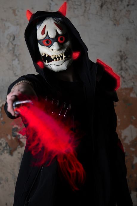 Character portrait in a horned demon mask and red hood, holding a red light