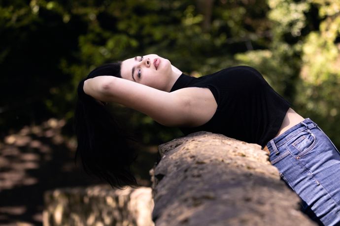Fashion photo of a woman in black leaning back on a sunlit rock