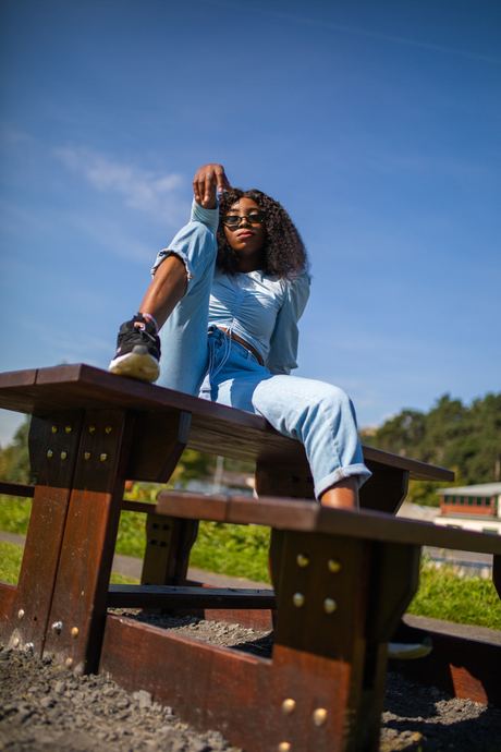 Fashion photo of a woman in a pale blue outfit sitting on a picnic table under a blue sky