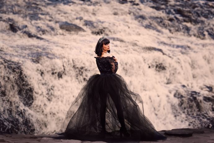 Fashion photo of a woman in a black tulle gown on rocks beside a waterfall