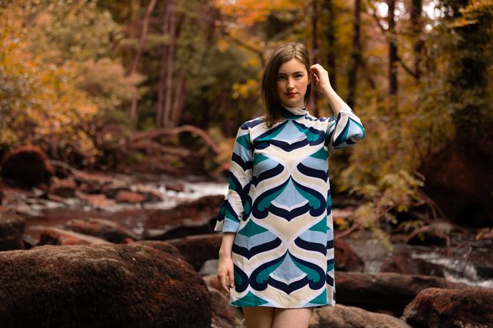 Fashion photo of a woman in a blue and white patterned dress by a river in autumn woodland
