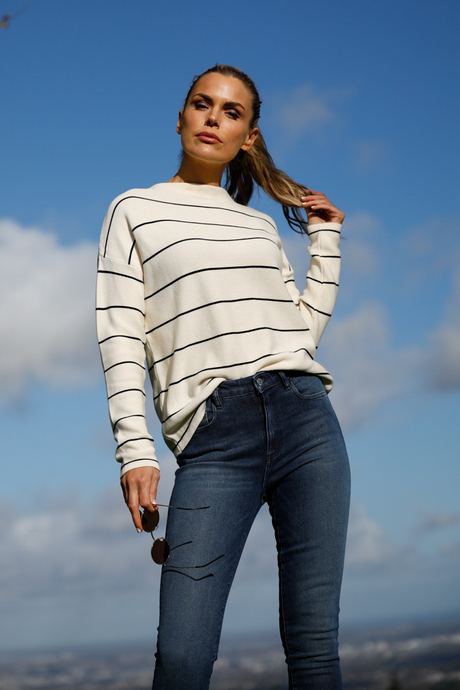 Fashion photo of a woman in a striped jumper and jeans against a blue sky