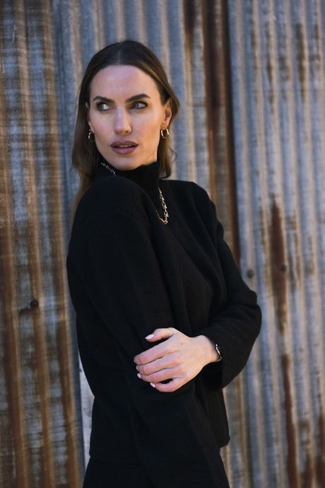 Fashion photo of a woman in a black coat beside a weathered wooden wall
