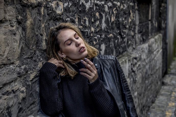 Fashion photo of a woman in a black leather jacket against an old stone wall