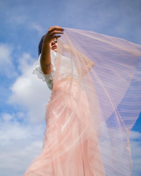 Fashion photo of a woman with a sheer pink veil lifted against a blue sky