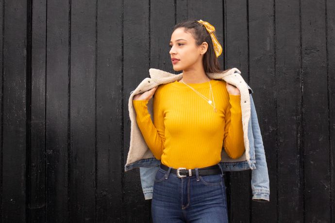 Fashion photo of a woman in a yellow jumper and denim jacket against a black wooden wall