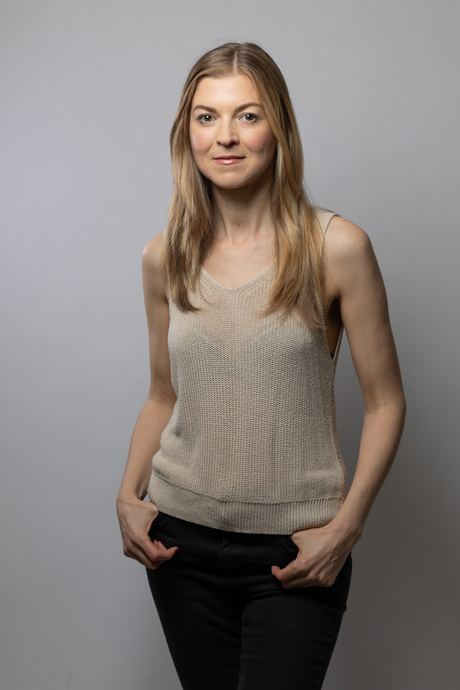 Portrait of a woman in a beige knit vest against a grey background