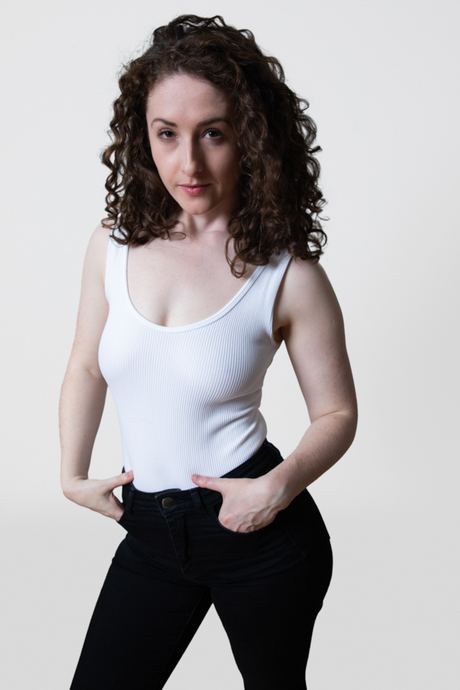 Portrait of a woman with curly hair in a white vest top and black jeans