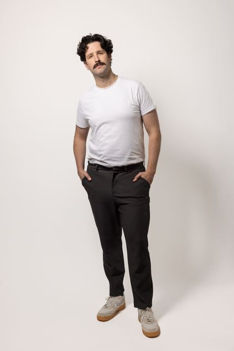 Full-length portrait of a man in a white T-shirt and dark trousers on a white background