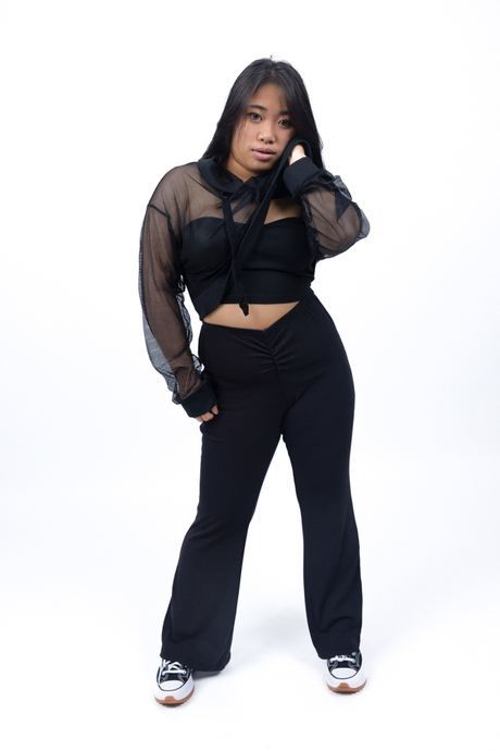 Full-length portrait of a woman in a sheer black top and black trousers on a white background