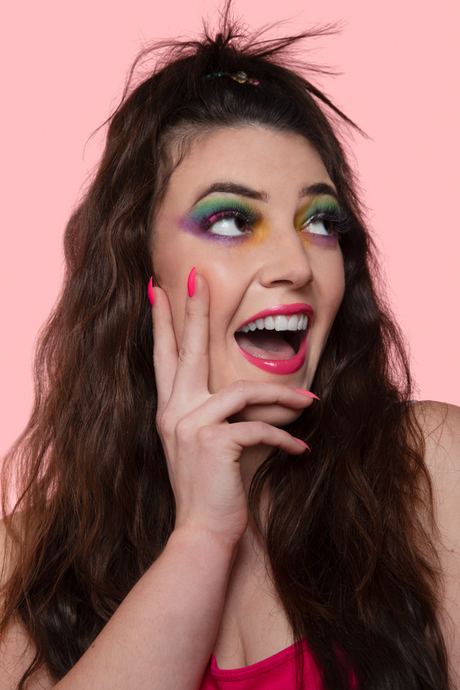 Portrait of a laughing woman with bold eye make-up against a pink background