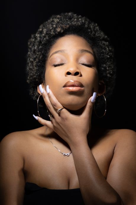 Portrait of a woman with eyes closed and hands near her chin on a dark background