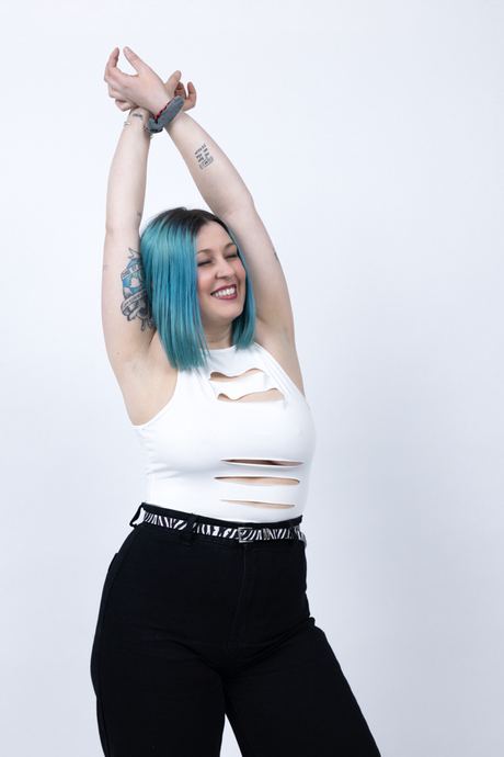 Portrait of a woman with blue hair and arms raised on a light background