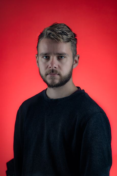 Headshot of a man in a navy jumper against a red background