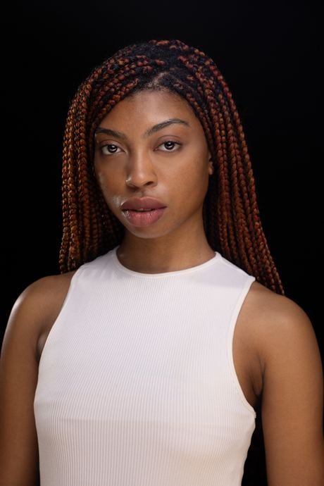 Portrait of a woman with long braided hair in a white top on a dark background